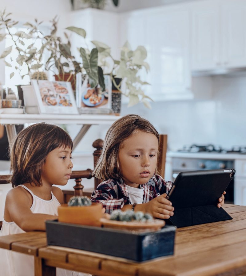 Little kid and his sister use digital tablet together in living room